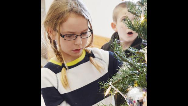 Malayne Condra, third grade, carefully places her ornament as her classmate, Tyler Cook, takes in the wonder of the class tree.